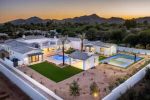 A sunset sky and a residence with a lawn, pools, and palm trees